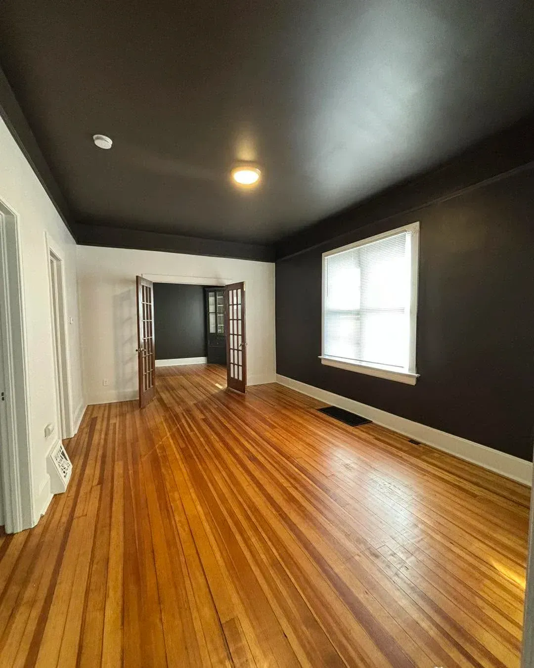 Empty room with dark walls, polished wood floors, and a window letting in daylight.